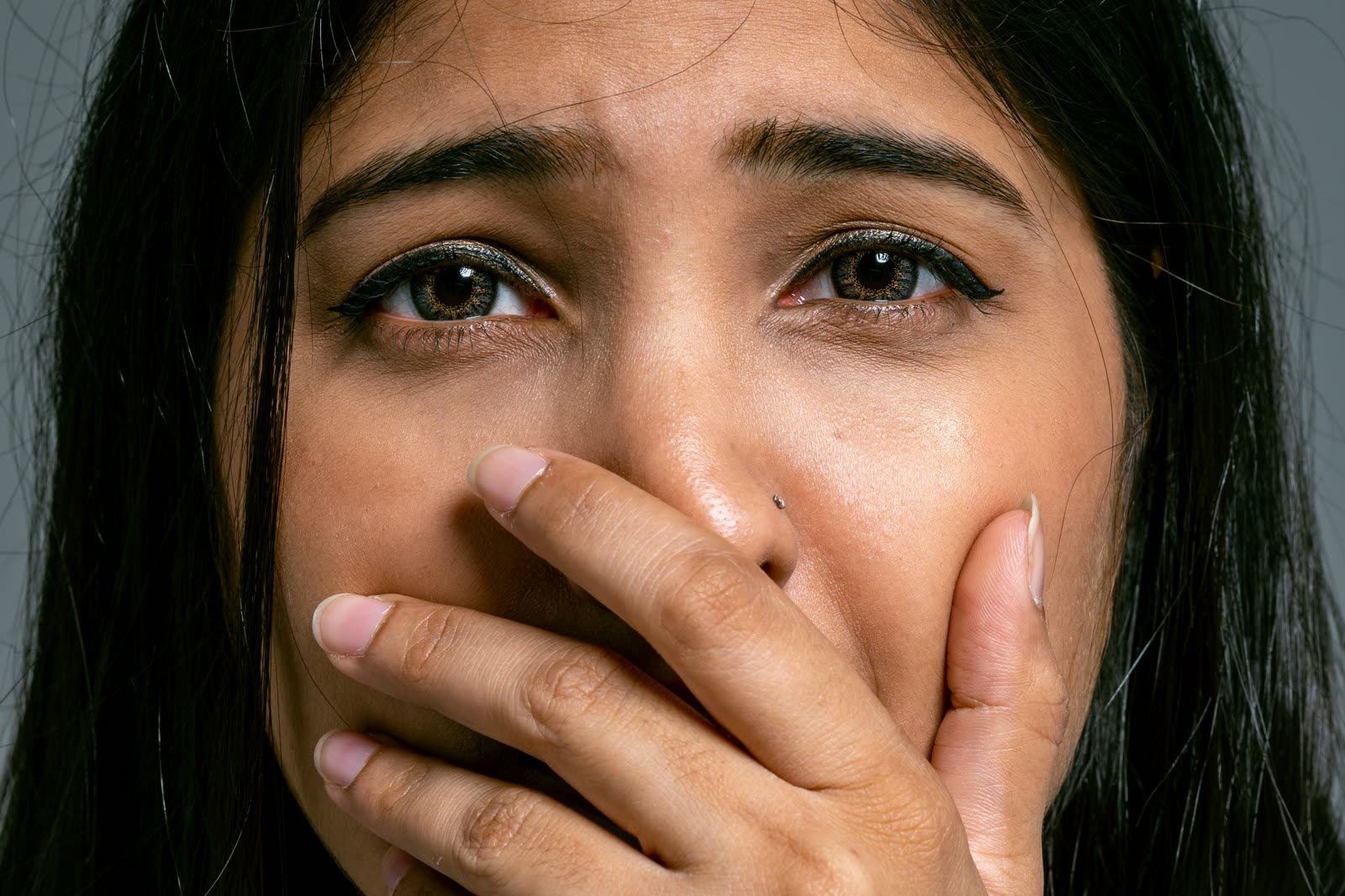 Primer plano del rostro de una mujer con la mano tapándose la boca y la mirada asustada