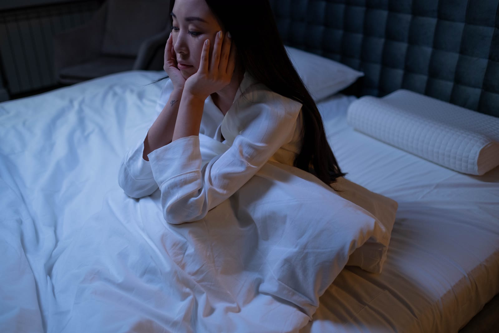 Una mujer despierta en la cama de noche, con las manos en la cara y la mirada perdida